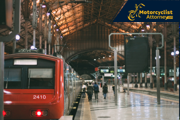 A train station with a red train stopped and pedestrians walking along the platform, symbolizing the railway setting where the San Leandro accident occurred. The image supports the report of a motorcyclist struck by a train during a group ride, as covered by Motorcyclist Attorney.