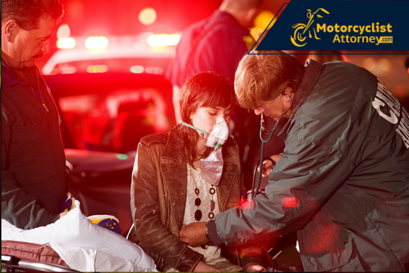 Una mujer herida recibe atención médica de emergencia con una mascarilla de oxígeno mientras paramédicos la asisten en el lugar de un accidente bajo luces rojas de patrullas. La imagen acompaña el informe del accidente mortal de motocicleta en Discovery Bay, posiblemente relacionado con DUI, como reporta Motorcyclist Attorney.