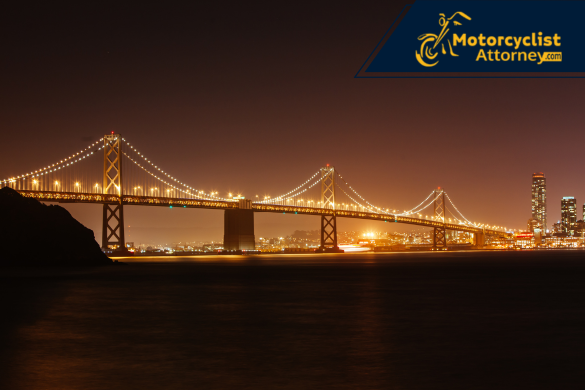 Vista nocturna del Bay Bridge iluminado sobre la bahía de San Francisco, simbolizando el lugar del accidente mortal de motocicleta con fuga que cobró la vida de un conductor. La imagen acompaña el reporte de Motorcyclist Attorney sobre el trágico incidente y la búsqueda del conductor responsable.