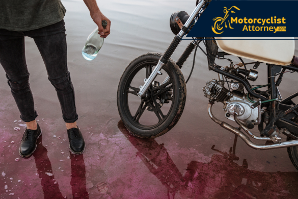 Hombre de pie junto a motocicleta sosteniendo una botella, con reflejos en el suelo mojado, simbolizando el peligro de conducir bajo los efectos del alcohol. Imagen ideal para casos legales de DUI en California.